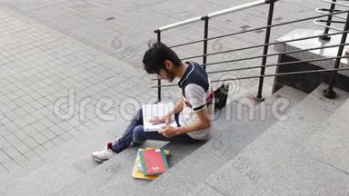 一位快乐的亚裔男学生坐在楼梯上<strong>看书</strong>的<strong>肖像</strong>