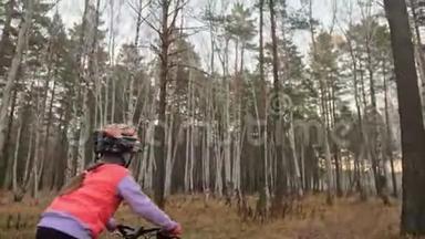 一<strong>个</strong>高加索儿童在秋季公园骑自行车。 小女孩骑着黑色橙色的自行车在森林里。 孩子是干的