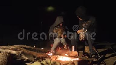 孩子们微笑，孩子们喝茶，青少年坐在篝火旁的生活方式，晚上篝火。 旅行徒步旅行冒险露营