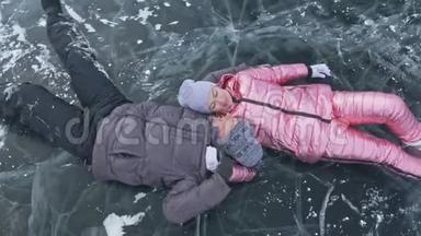 在冰封的湖面上，年轻夫妇在冬天散步时玩得很开心。 恋人们躺在冰面上，有裂缝
