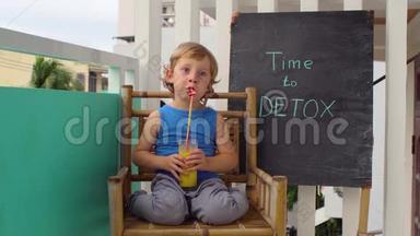 时间到DETOX粉笔铭文。 这个男孩正在喝新鲜、健康、排毒的水果饮料。 奶昔，新鲜果汁，牛奶