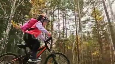 一个高加索儿童在秋季公园骑自行车。 小女孩骑着黑色橙色的自行车在森林里。 孩子是干的