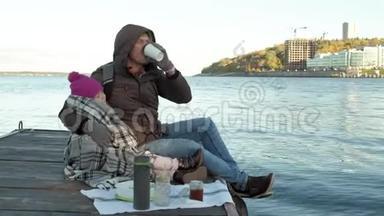 男人和<strong>女孩</strong>，父亲和女儿，坐在河港，<strong>喝茶</strong>，野餐，笑，穿着暖和的衣服