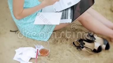 一个忙碌的年轻女子正在用一台手提电脑，手里<strong>拿</strong>着商业文件，<strong>拿起</strong>一个电话，坐着打电话
