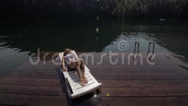 女人躺在日光浴床上，戴着太阳镜和一条薄纱披肩。 女孩在洪水木水下码头休息。 路面是