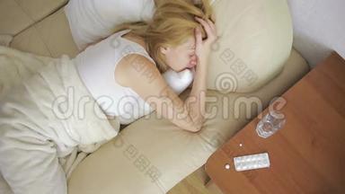 生病的女人躺在床上。 药丸和一杯水。 喝药片。 止痛药