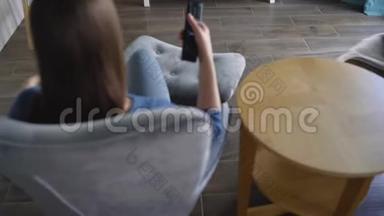 女人坐在椅子上，用绿色的屏幕看电视，用遥控器切换频道。 铬键