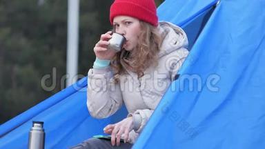 漂亮的女游客戴着红帽子坐在旅游帐篷里，<strong>喝</strong>着<strong>热水</strong>瓶里的茶