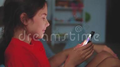 有智能手机的小女孩躺在床上睡觉。 在家里上网玩智能手机网络游戏的小女孩