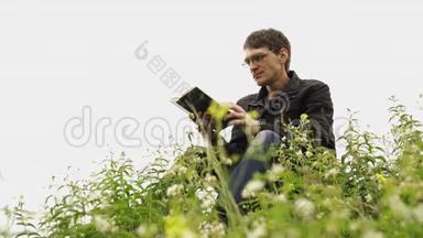 人在绿色丘陵田里<strong>看书</strong>.. 年轻英俊的男子戴着眼镜，穿着暖和的夹克，在露天<strong>看书</strong>