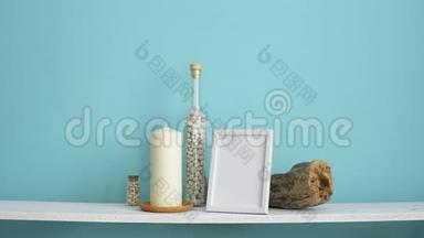 现代客房装饰与相框模型。 白色架子靠在粉彩绿松石墙上，瓶子里有蜡烛和岩石。 手