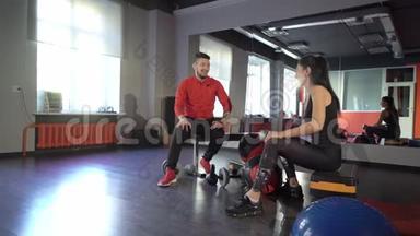 在健身房里，一个年轻、健康、运动活跃的身材女孩，旁边有一位英俊、乐于助人的私人教练。
