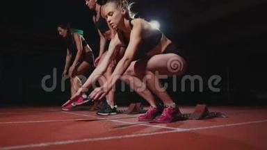 田径场的女跑运动员在比赛前蹲在起点。 动作缓慢。