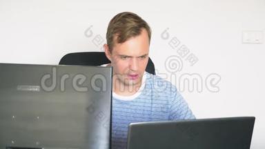 一个男人坐<strong>在家</strong>里的<strong>办公</strong>桌前，<strong>在家</strong>里的电脑和笔记本电脑里工作。