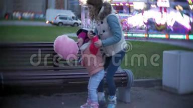 美丽的小女孩坐在游乐园的长凳上，吃着滚滑轮滑冰鞋上滚来滚去的粉红色甜棉糖