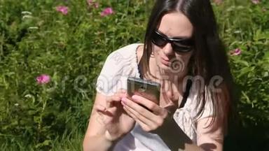 在阳光明媚的日子里，坐在公园里的女人正在用手机输入一条信息。