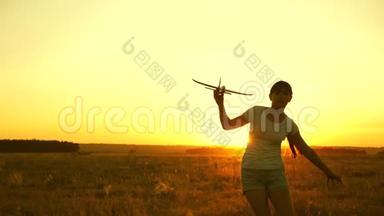快乐的女孩带着玩具飞机在夕阳下的田野上奔跑。 孩子们玩玩具飞机。 青少年的梦想