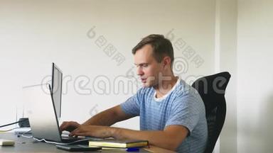 一个男人坐在家里的办公桌前，在家里的电脑和笔记本电脑里工作。