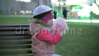 美丽的小女孩坐在<strong>游乐园</strong>的长凳上，吃着滚滑轮滑冰鞋上滚来滚去的粉红色甜棉糖