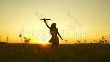 快乐的女孩带着玩具飞机在夕阳下的田野上奔跑。 孩子们玩玩具飞机。 青少年的梦想