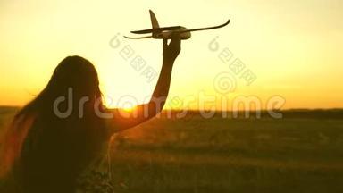 快乐的女孩带着玩具飞机在夕阳下的田野上奔跑。 孩子们玩玩具飞机。 少年梦想