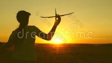 孩子们玩玩具飞机。 快乐的女孩带着玩具飞机在夕阳下的田野上奔跑。 少年梦想