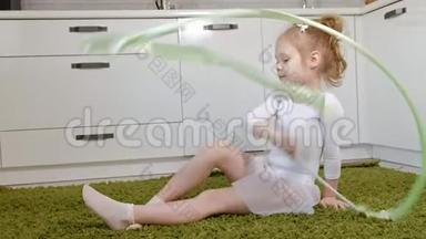 一个快乐的小女孩穿着白色体操泳衣训练，用丝带跳舞，进行艺术体操，跳跃和