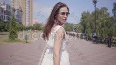 肖像迷人的年轻女孩戴着太阳镜和一件白色的<strong>夏季</strong>时装<strong>长裙</strong>走在户外。 休闲
