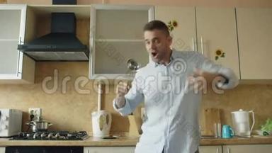 有魅力的年轻风趣男子在家厨房做饭时用瓢泼大雨跳舞唱歌