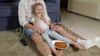 男人和女儿看电视，坐在地上吃零食