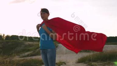 超级英雄女孩穿着红色斗篷站在<strong>战</strong>场上，斗篷在风中飘扬。 慢动作。 美丽的女孩<strong>梦想</strong>