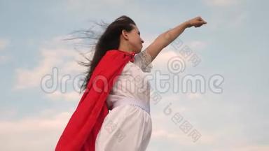 美丽的超级英雄女孩站在一片红色斗篷的田野上，斗篷在风中飘扬。 女孩<strong>梦想</strong>成<strong>为</strong>一个