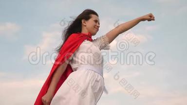 美丽的超级英雄女孩站在一片红色<strong>斗篷</strong>的田野上，<strong>斗篷</strong>在风中飘扬。 女孩梦想成为一个