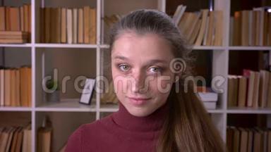 一幅年轻的白种人女学生的特写照片，她开心地笑着看着<strong>室内图</strong>书馆的摄像机