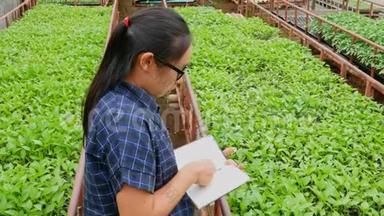 农民亚洲妇女在温室里工作，带着笔记本检查农场上<strong>生长</strong>的<strong>幼苗</strong>和温室里的疾病。