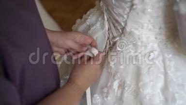 伴娘帮助年轻新娘穿上婚纱。 豪华婚纱