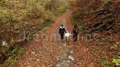 一位年轻的母亲带着她的两个孩子走过秋天的森林。 他们沿着森林小径走。 他们很开心