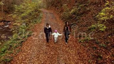 一位年轻的母亲带着她的两个孩子走过秋天的森林。 他们沿着森林小径走。 他们很开心