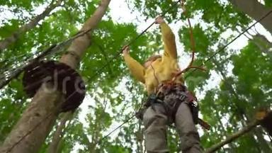 一个戴<strong>安全带</strong>的小男孩在森林探险公园的树梢上攀爬。他在高绳道上攀爬