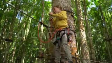 一个穿着安全装备的小男孩爬上森林探险公园的一条路线。 他爬在高绳上. 室外