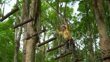 一个戴安全带的小男孩在森林探险公园的树梢上攀爬。他在高绳道上攀爬