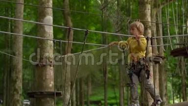 一个戴安全带的小男孩在森<strong>林探</strong>险公园的树梢上攀爬。他在高绳道上攀爬