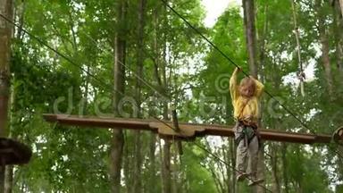 一个戴安全带的小男孩在森<strong>林探</strong>险公园的树梢上攀爬。他在高绳道上攀爬