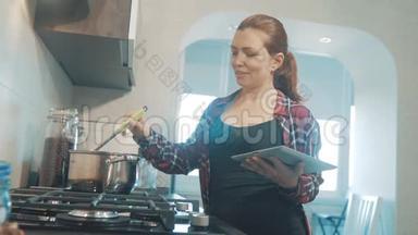 女人在厨房煮汤锅，防止锅里的水，看看数字平板上的食谱。 妇女