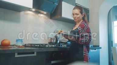 女人在厨房<strong>煮汤</strong>锅，防止锅里的水，看看数字平板上的食谱。 妇女