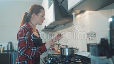 女人在<strong>厨房</strong>煮汤<strong>锅</strong>，防止<strong>锅</strong>里的水，看看数字平板上的食谱。 妇女