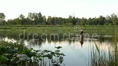 渔夫在一条平静的河里钓鱼。 一个穿着渔具的人在河里站着扔一根鱼竿