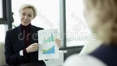 一位女经理在会议上向同事介绍新的项目计划，并向同事解释挂图上的想法