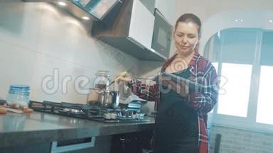 女人在厨房煮汤，防止锅中的水，看看数字平板上的食谱。 妇女