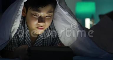 小男孩在床上玩手机或智能手机。 夜晚